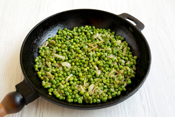 Homemade Sauteed Green Peas in a cast-iron pan on a white wooden background, side view.