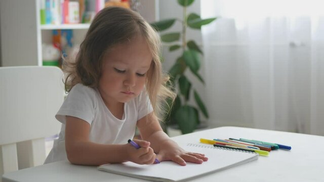 Cute toddler girl draws with felt-tip pens. Portrait of toddler girl at home.