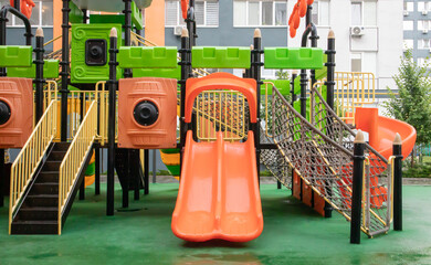 Fototapeta na wymiar A courtyard of high-rise buildings with a new modern colorful and large playground on a rainy summer day without people. Empty outdoor playground. A place for children's games and sports.