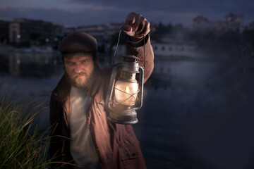 a man in defocus with an evil face with a beard and in vintage clothes holds a kerosene lamp in his...