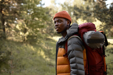 Afro american guy walking alone on forest path. Guy hiking with backpack in trees. Explore virgin...