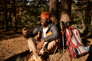 Happy black guy talking to family on video conference. Chilling on fresh air, weekend in forest for...