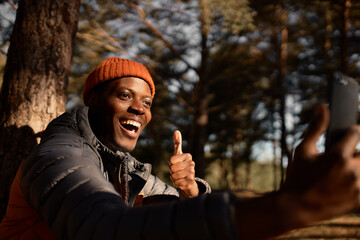 Cheerful and happy man showing thumps up talking on face time. Connection with people on distance, see your family on camping in forest. Technology, communication, emotion, fun concept. Copy space