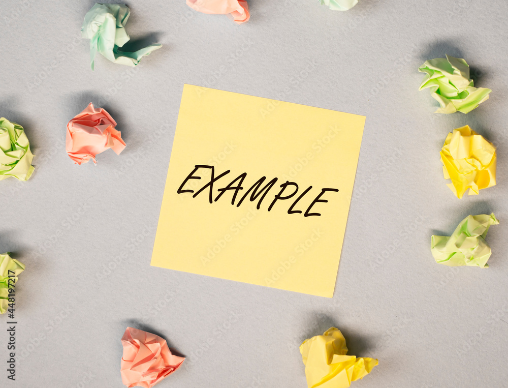 Poster example word on yellow note on gray background with crumpled papers around, top view.
