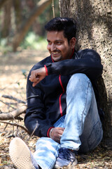 The Handsome guy, sitting or standing and leaning on tree in the forest. Handsome young man looking at someone