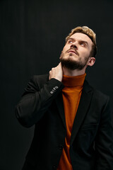  young blond man in jacket orange sweater on dark background raised his head up