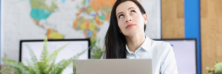 Naklejka premium Pensive young woman sits at laptop and looks up