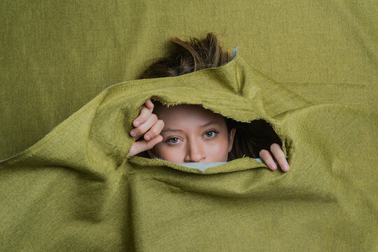 Young Woman Peeking Out Of Green Ripped Fabric