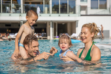 Fototapeta na wymiar Happy family, parents playing with the kids, mother and daughter in the swimming pool