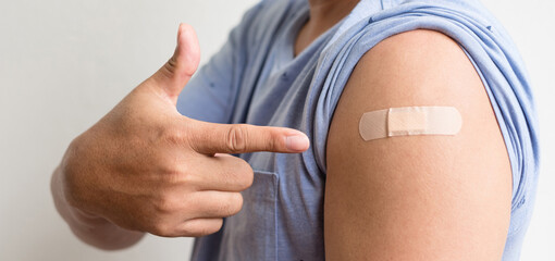 Asian man shows plaster on her shoulder after being vaccinated against Covid-19. Coronavirus vaccination campaign concept - obrazy, fototapety, plakaty