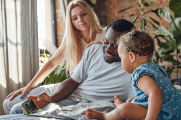 Leisure time of multiethnic family lying on bed with phone