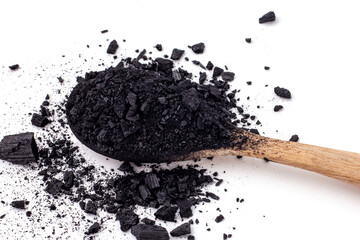 Close up of small pieces of charcoal and charcoal powder was placed on a wooden spoon and scattered on a white background.