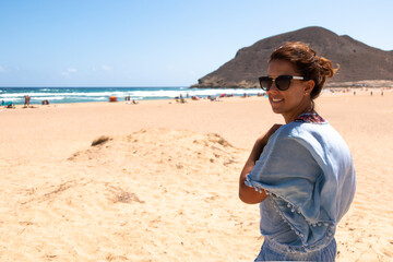 Young woman smiling with sunglasses in a beach on a summer day