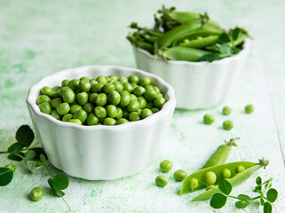 Fresh green peas pods and green peas with sprouts on green wooden background.