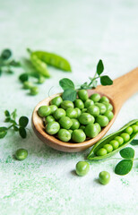 Fresh green peas pods and green peas with sprouts on green wooden background.