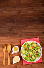 Big white bowl of lettuce, sprout salad with boil egg, and tomato mix with sesame dressing on red polka dots fabric above wooden table and small olive oil jar, sesame cup and utensil beside