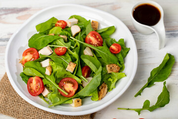 Fresh spinach salad with tomato, small pieces of herb roasted chicken in white ceramic dish on brown sackcloth, together with balsamic vinegar on white wooded table. Concept for healthy