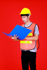 Asian engineer wearing safety suit and safety helmet standing look at file folder with happy and confident holding folder paper document on hand.Shoot in studio with red background