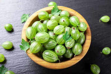 Fresh gooseberries in wooden bowl on black stone slate background.
