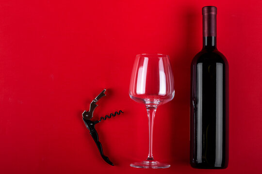 Bottle of red wine and an empty wine glass with a corkscrew next to it. Composition on a red background. Romantic mood. Space for text.