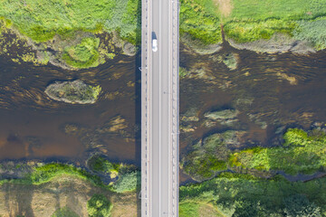 Aerial top down view of car driving over bridge. River flowing under bridge