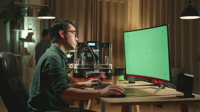 Frustrated Asian Man Work On 3D Printer And Personal Computer With Mock Up Green Screen Display In Home Office
