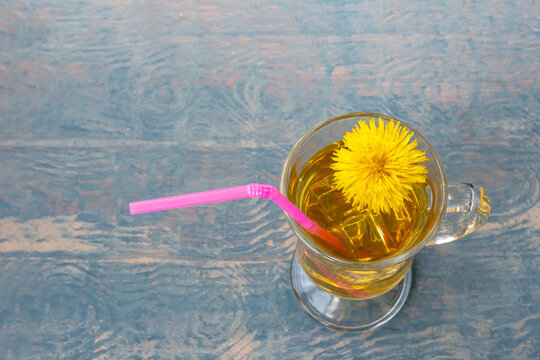 Cup Of Tea With Herbal Tea And Yellow Dandelion And Pink Straw On Blue Wooden Background Illuminated By Sunbeam