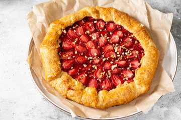 French galette or pie with strawberries and almonds on baking paper on a light gray culinary background closeup. Summer homemade sweet pastries