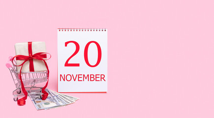 A gift box in a shopping trolley, dollars and a calendar with the date of 20 november on a pink background.