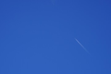 Airplane flying high up and leaving white traces or contrail behind. There is a lot of copy space on the blue sky on the background. 