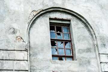 The facade of an old house with broken windows. Gray wall with decorative arch and wooden window frame. Flat lay frame
