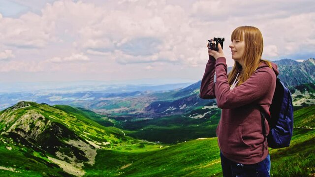 A beautiful woman in the mountains hiking, exploring nature and take a photo with the camera, take pictures of landscape nature around her