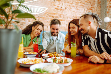 Happy friends having a great time in cafe. Young people sitting in a restorane having fun together, laughing, drinking cocktails and eating. Friendly dinner.