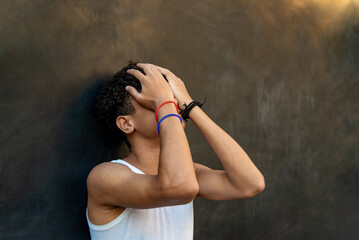 Afro latin male teenager against a wall clutching his head