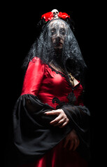 Witch or sorceress in red gothic dress, black bridal veil and crown with skull and roses standing on black background. Halloween concept.