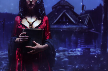 Witch or sorceress with runic makeup and wooden animal skull amulet holding a magic book standing...
