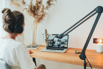 Back view on young woman recording podcast at home studio. Female podcaster recording broadcasting into microphone