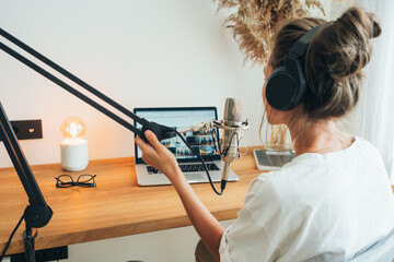 Woman working at home and talking into a microphone and recording podcast. Female working at...