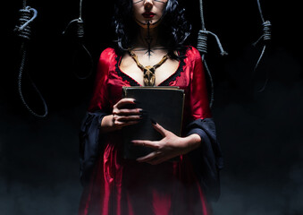 Witch or sorceress with runic makeup and wooden animal skull amulet holding a magic book on dark...