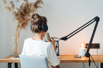 Back view on woman sits on table and recording podcast at his small cozy radio studio. Female...