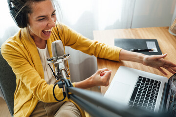 Charismatic woman radio host recording podcast at home studio. Female podcaster recording...