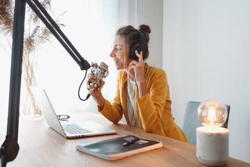Young female radio host recording and broadcasting her podcast from homemade studio. Woman...
