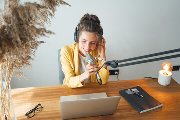 Woman podcaster streaming and broadcasting her podcast from homemade studio. Female recording podcast from home and talking into a microphone.