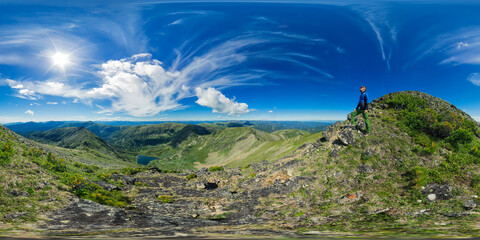Landscape panorama lake in the shape of a heart among high green mountains and a male climber, on a sunny summer day and cloudy sky. Spherical panorama 360vr