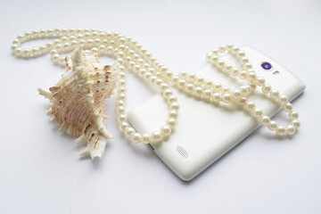 Photography in shades of white with a marine theme. A photograph of a seashell, a pearl necklace, and a white mobile phone.