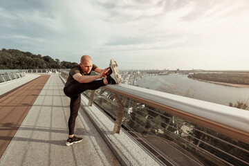 Fototapeta na wymiar Young European man stretches his legs on footbridge in the city. Healthy lifestyle concept. High quality photo