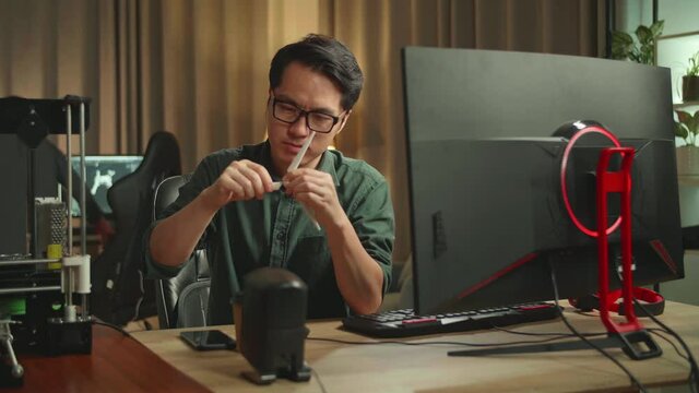 Asian Man Looking At Wind Turbine Model From 3D Printer And Works On Personal Computer, He Works At Night 
