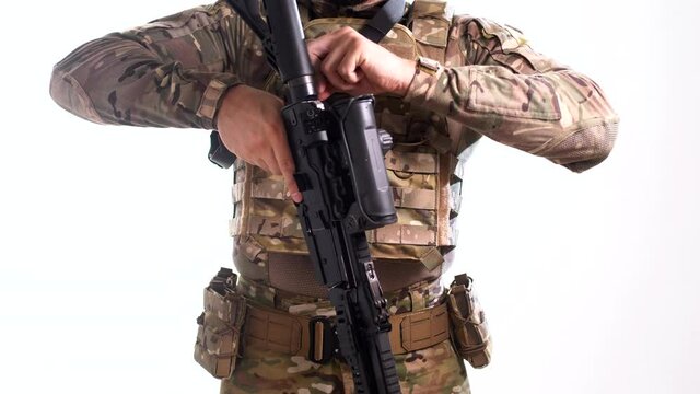 Special Forces scout in multicam tactical gear picks up a combat rifle and attaches it to his weapon belt. White background 