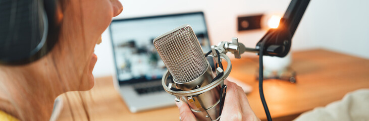 Young female radio host recording and broadcasting her podcast from home studio. Woman talk into...