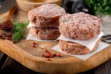 Frozen spicy pork patties with seasonings on wooden board. Butcher minced meat cutlet, close up